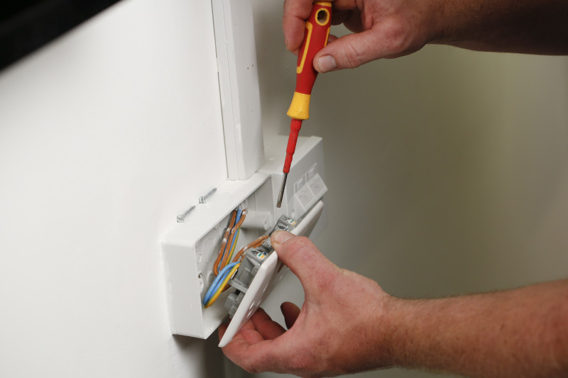 An electrical socket being repaired with an insulated screwdriver